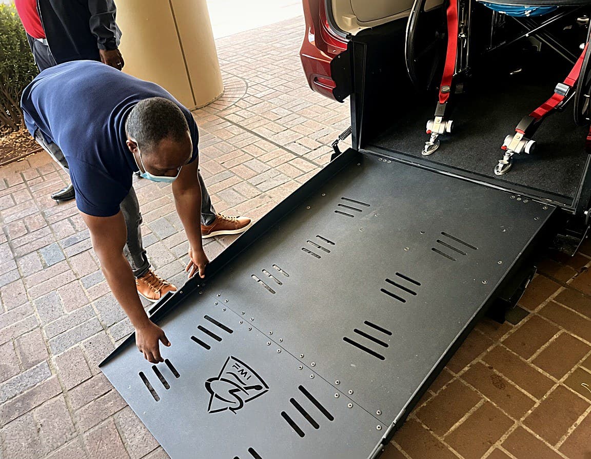 A BridgeWell driver lowering the ramp at the open rear of an accessible van.